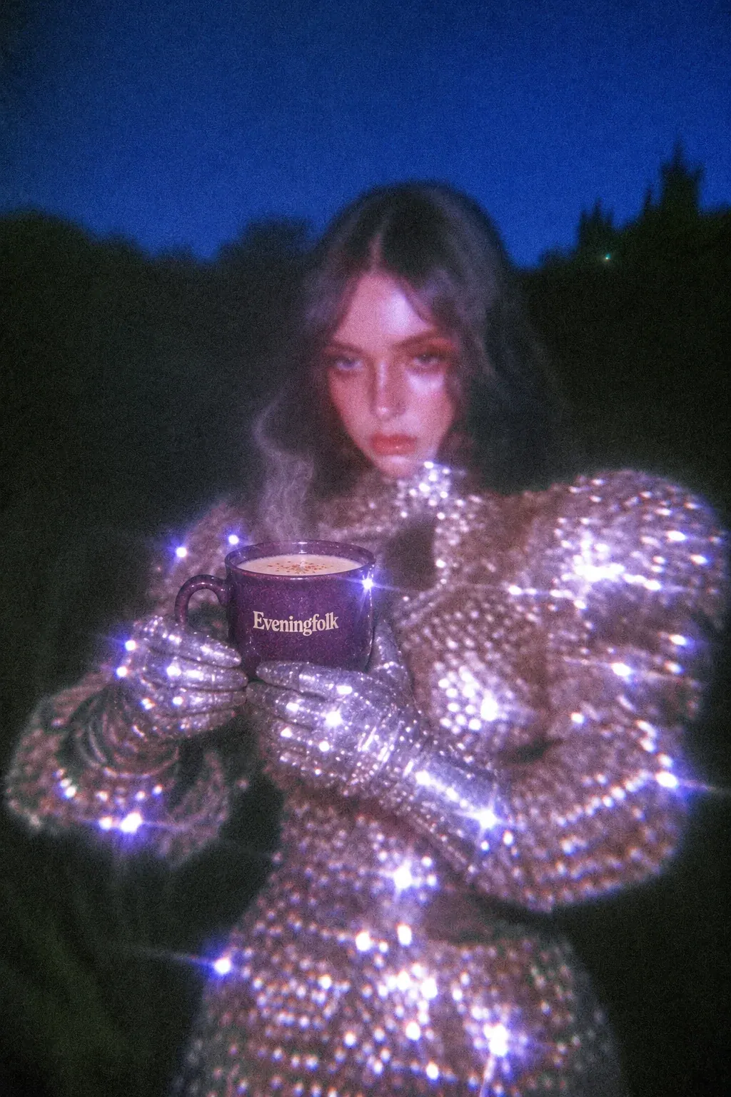 A woman in shimmering silver armor holding an Eveningfolk mug beneath a blue evening sky